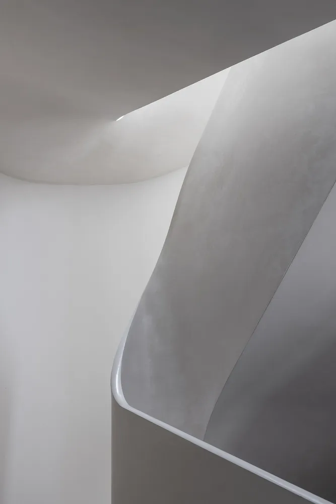 Modern architectural staircase featuring curved concrete design and white walls.