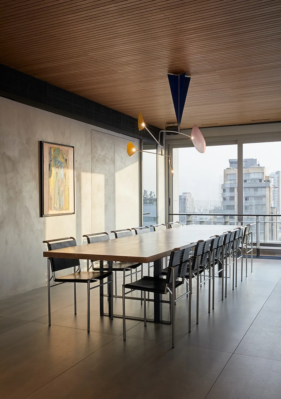 Modern office space featuring a long wooden table surrounded by black chairs, with a contemporary chandelier overhead and a l