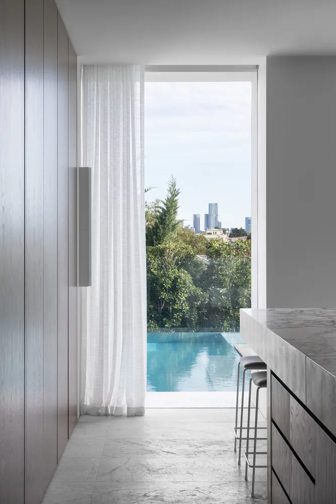 A modern residential space featuring a glass window overlooking a swimming pool surrounded by greenery and cityscape.