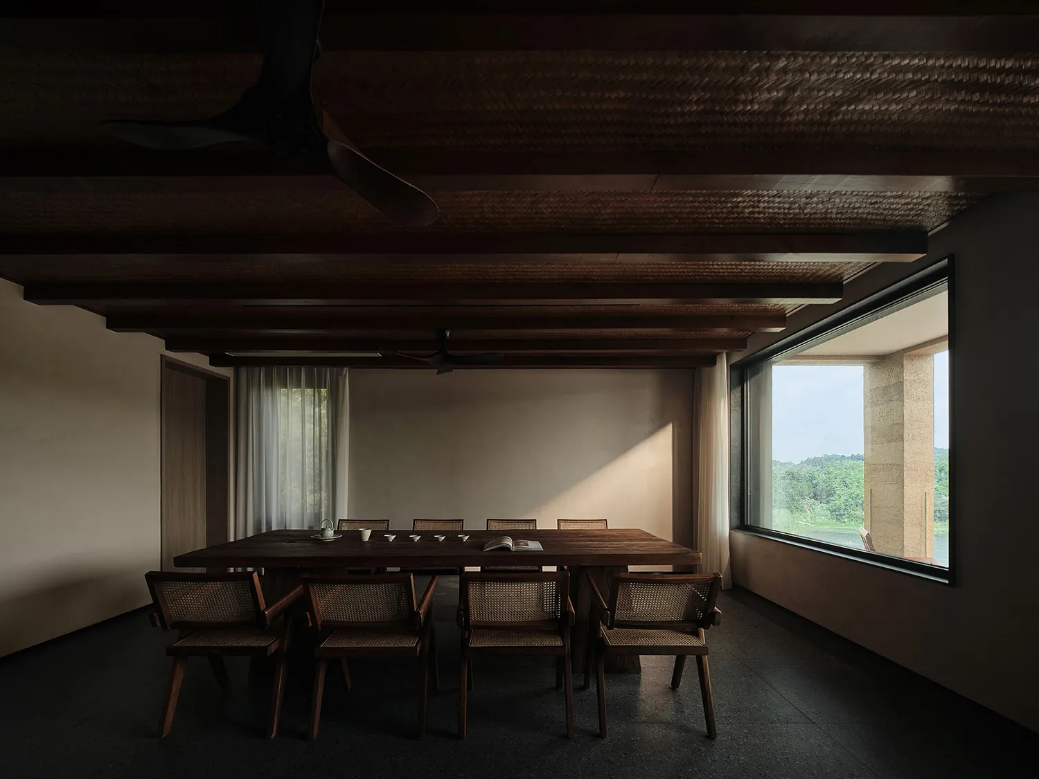 A minimalist residential dining room featuring wooden furniture, large windows, and a natural light setting.