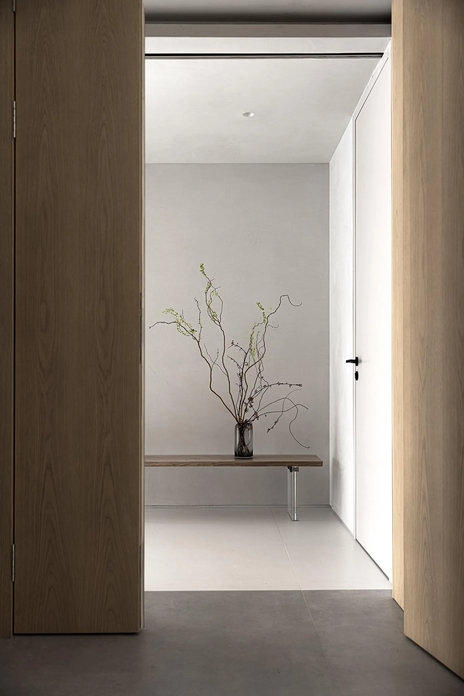 Minimalist entryway featuring wooden bench and concrete floor.