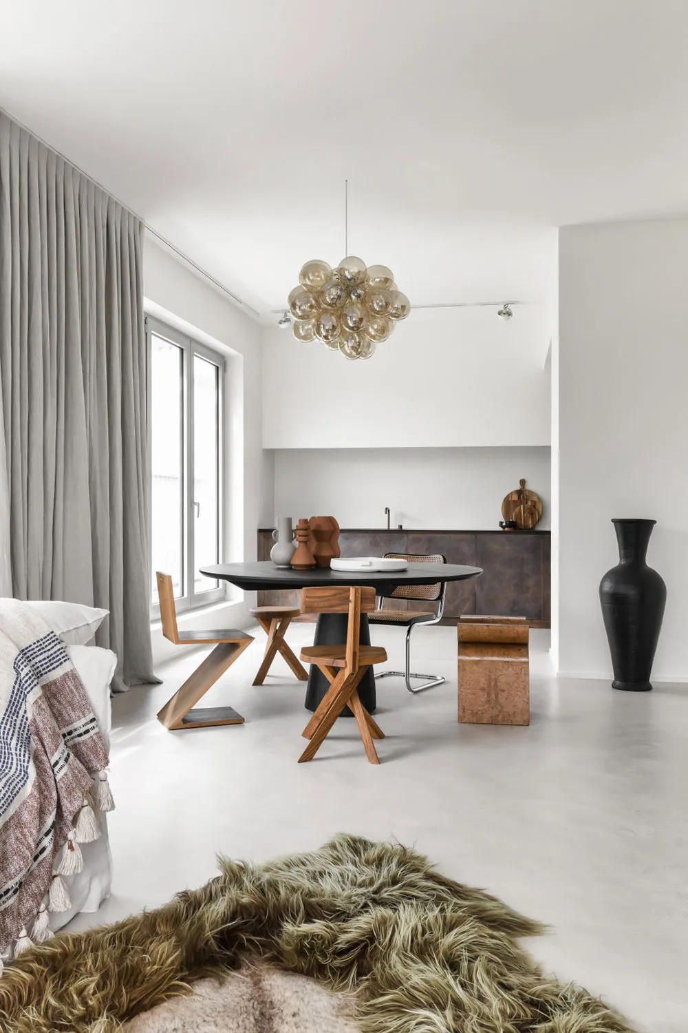 A minimalist dining room featuring modern furniture, including a round wooden table, wooden chairs, and decorative elements.