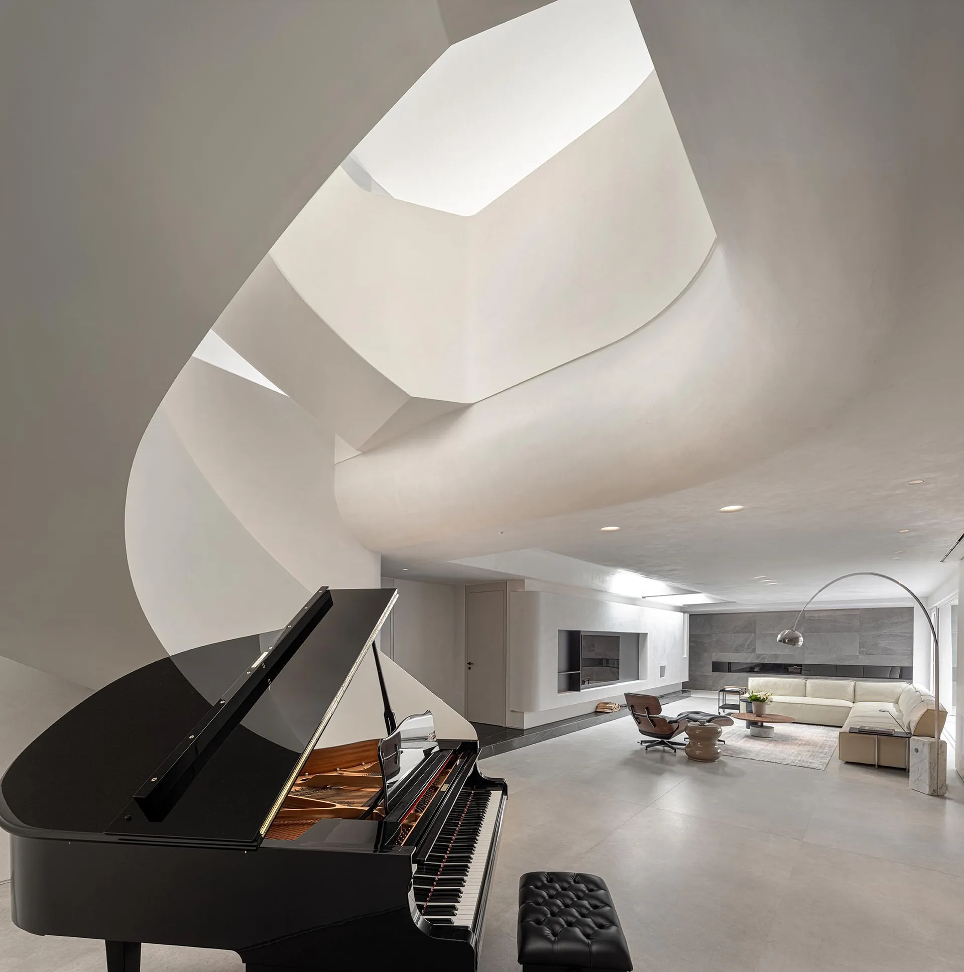 A spacious, minimalist residential interior with concrete walls, a grand piano, and a modern fireplace.