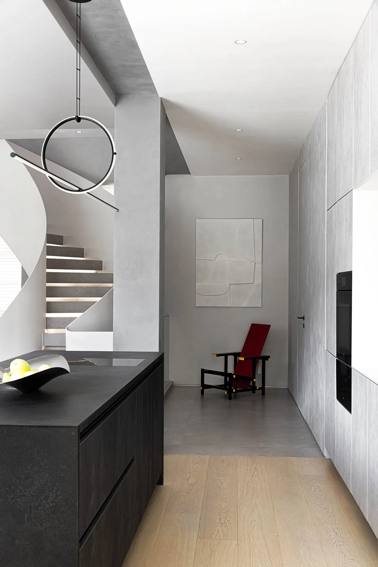 A modern kitchen with a concrete counter top, red chair, and abstract wall art.