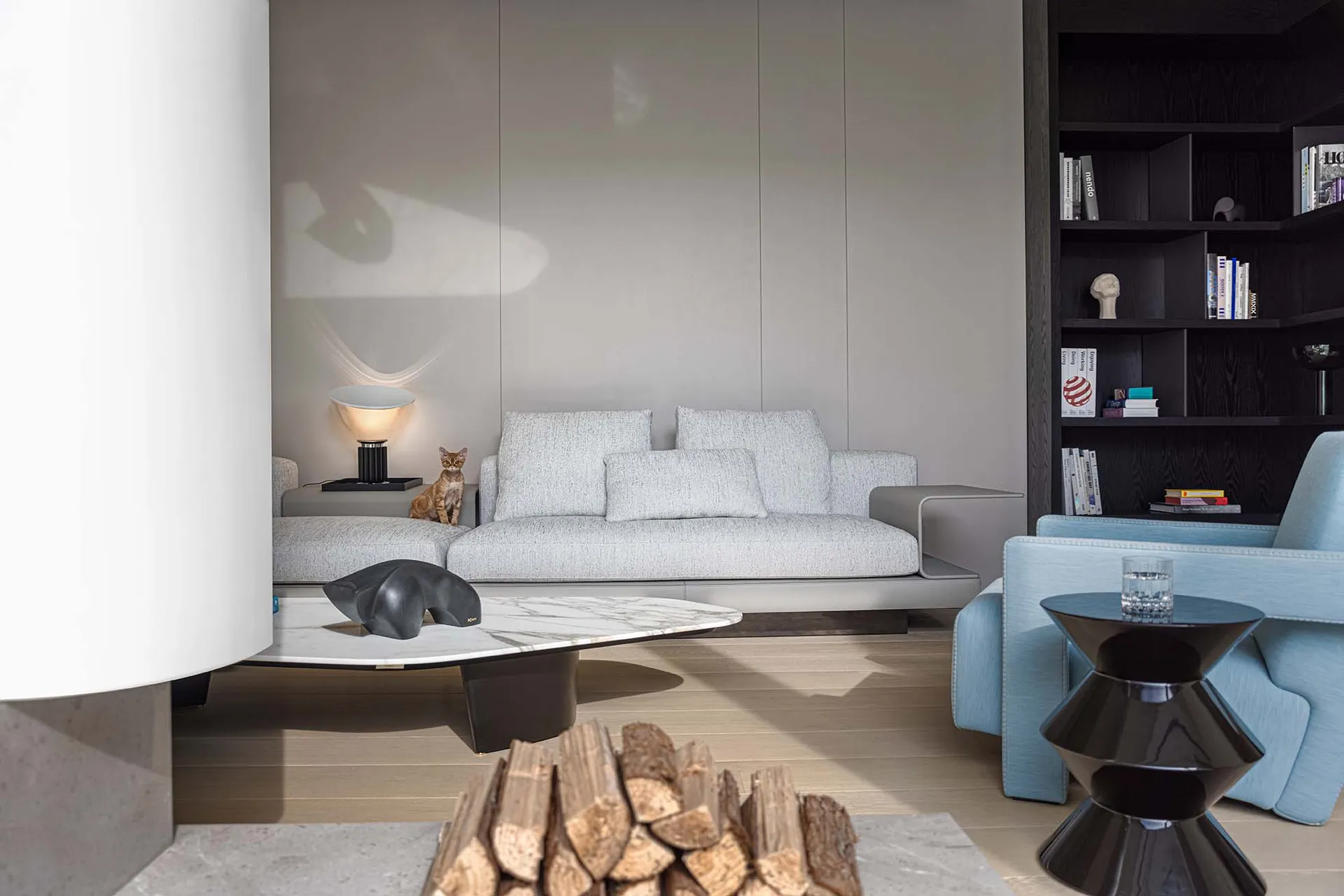 A modern living room featuring a light-colored couch, a table lamp, and a tall bookshelf filled with books.
