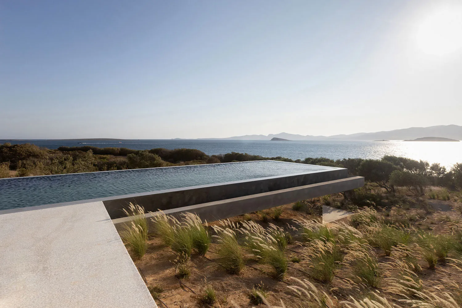 Modern floating concrete infinity pool overlooking the ocean and mountains.