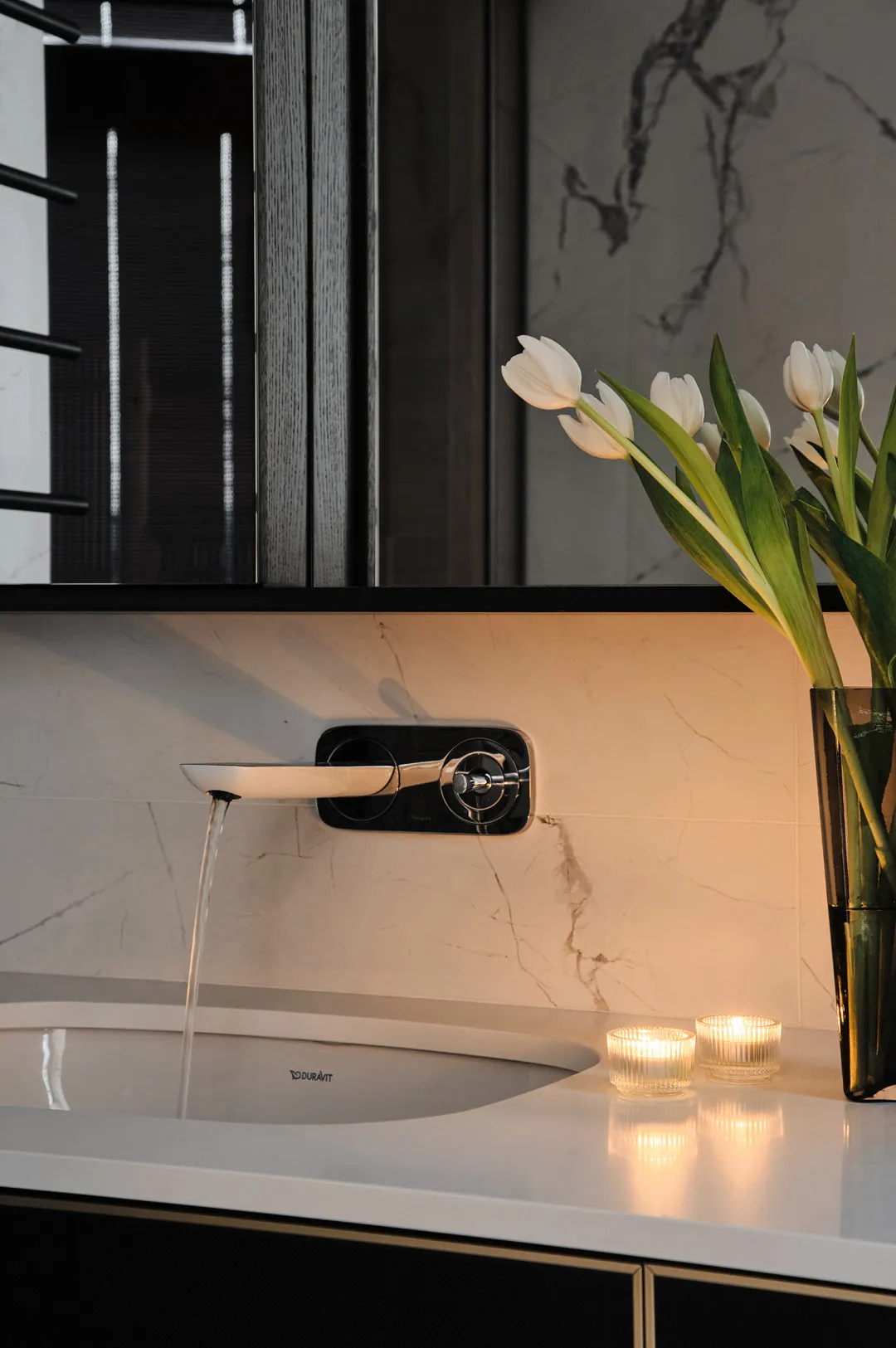 Modern bathroom interior featuring a sink with a wall-mounted faucet and white tulips in a vase, with ambient lighting and ma