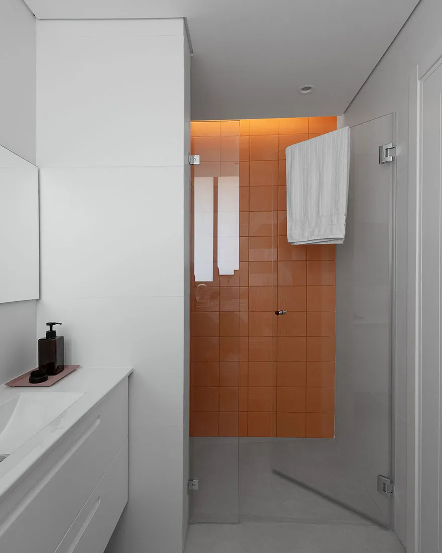 Modern bathroom featuring orange tiled walls and white fixtures and cabinetry.