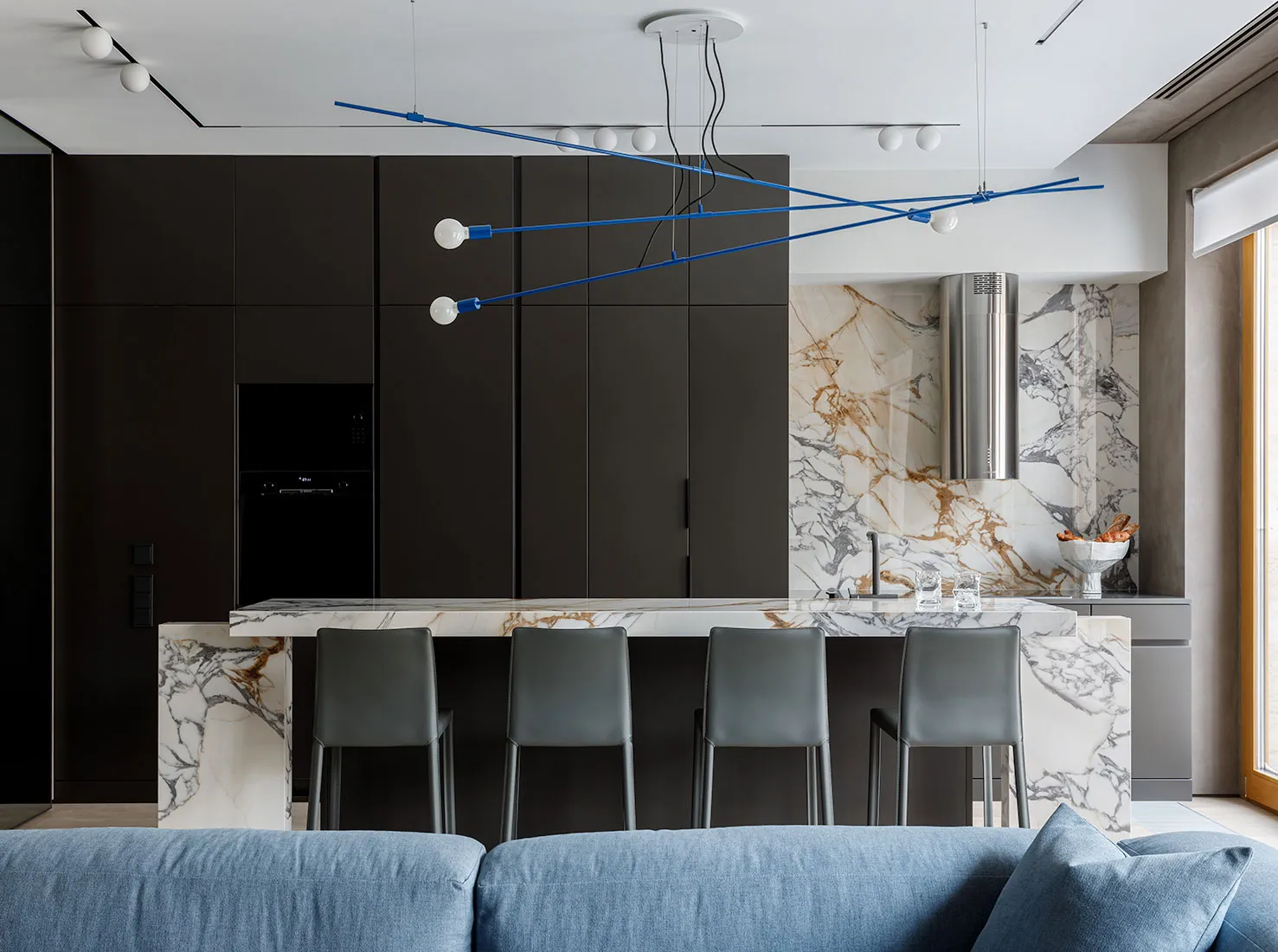 Modern kitchen featuring a marble countertop with a steel range hood and black cabinetry.