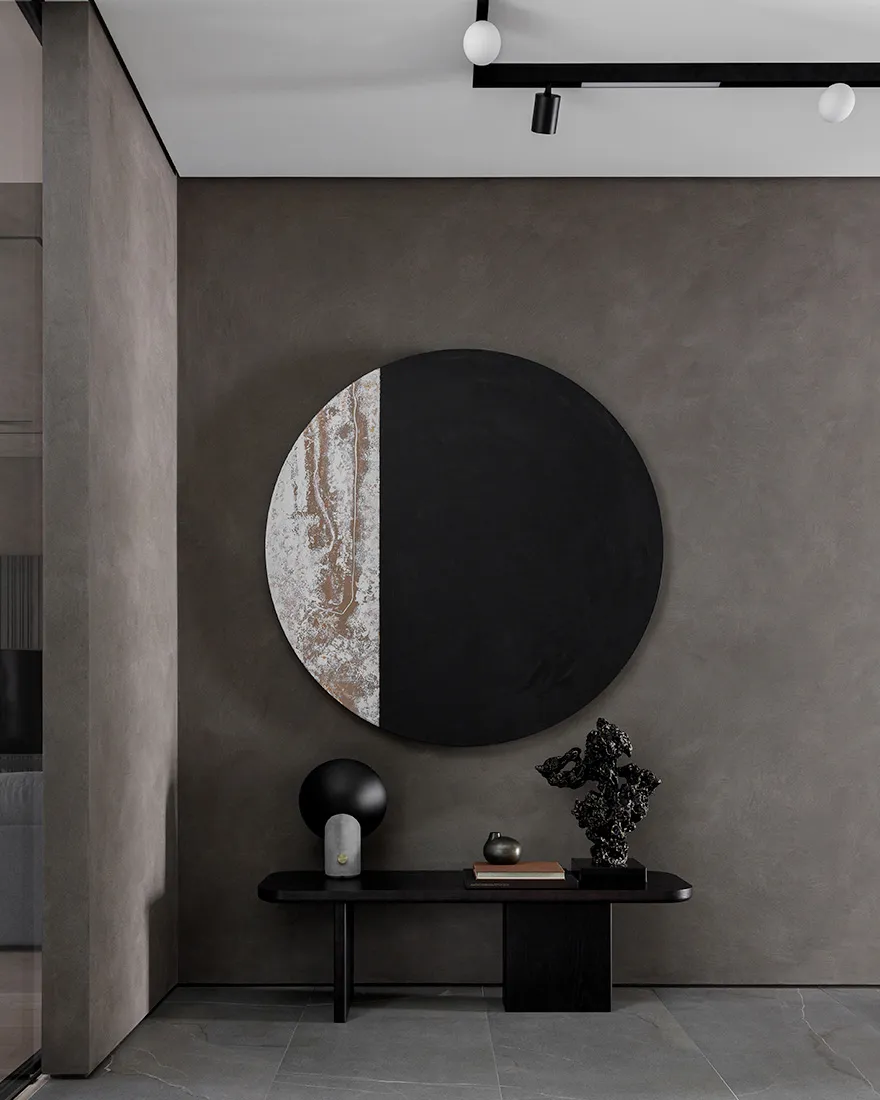 A minimalist entrance lobby featuring a metal table with various decorative items and a large circular artwork with a black a