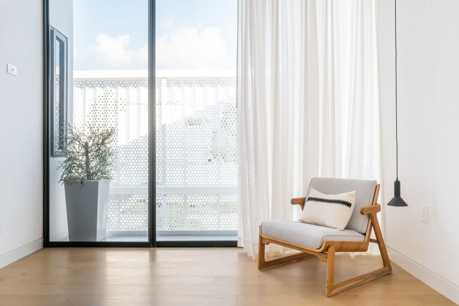 Modern minimalist living room with a wooden armchair, white curtains, and a large window.