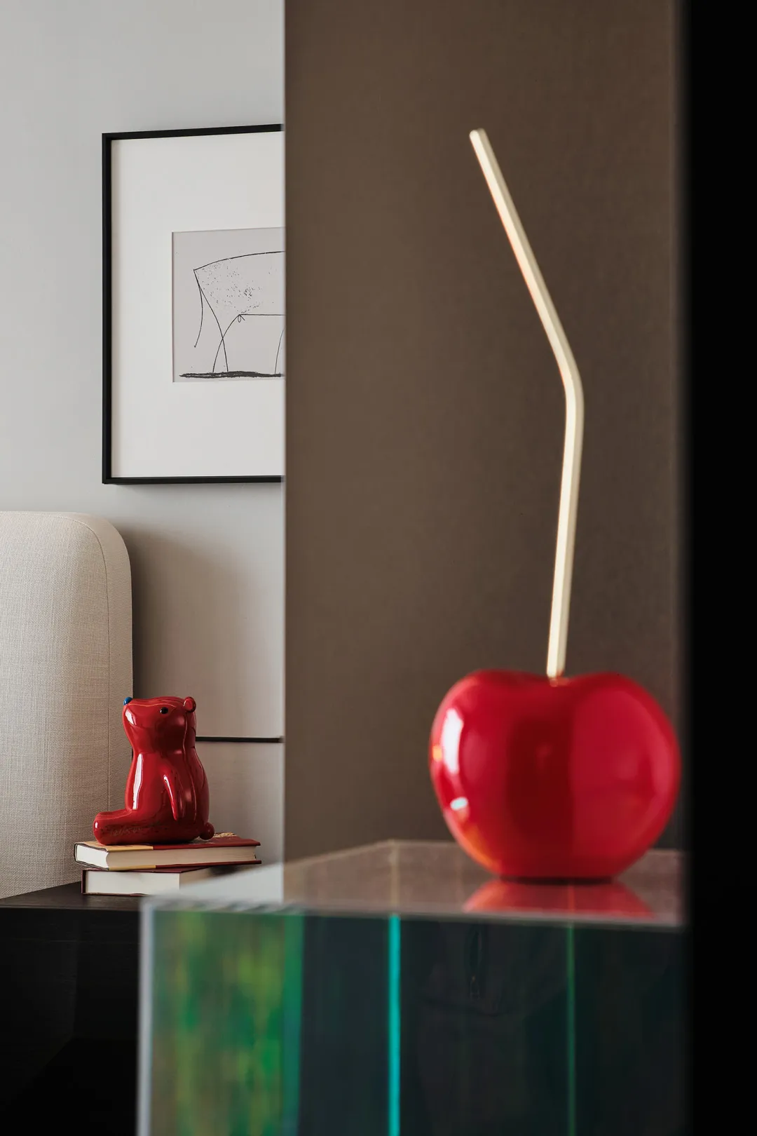 A modern, red ceramic apple with a gold stem placed on a glass surface, surrounded by a minimalist decorative setting.
