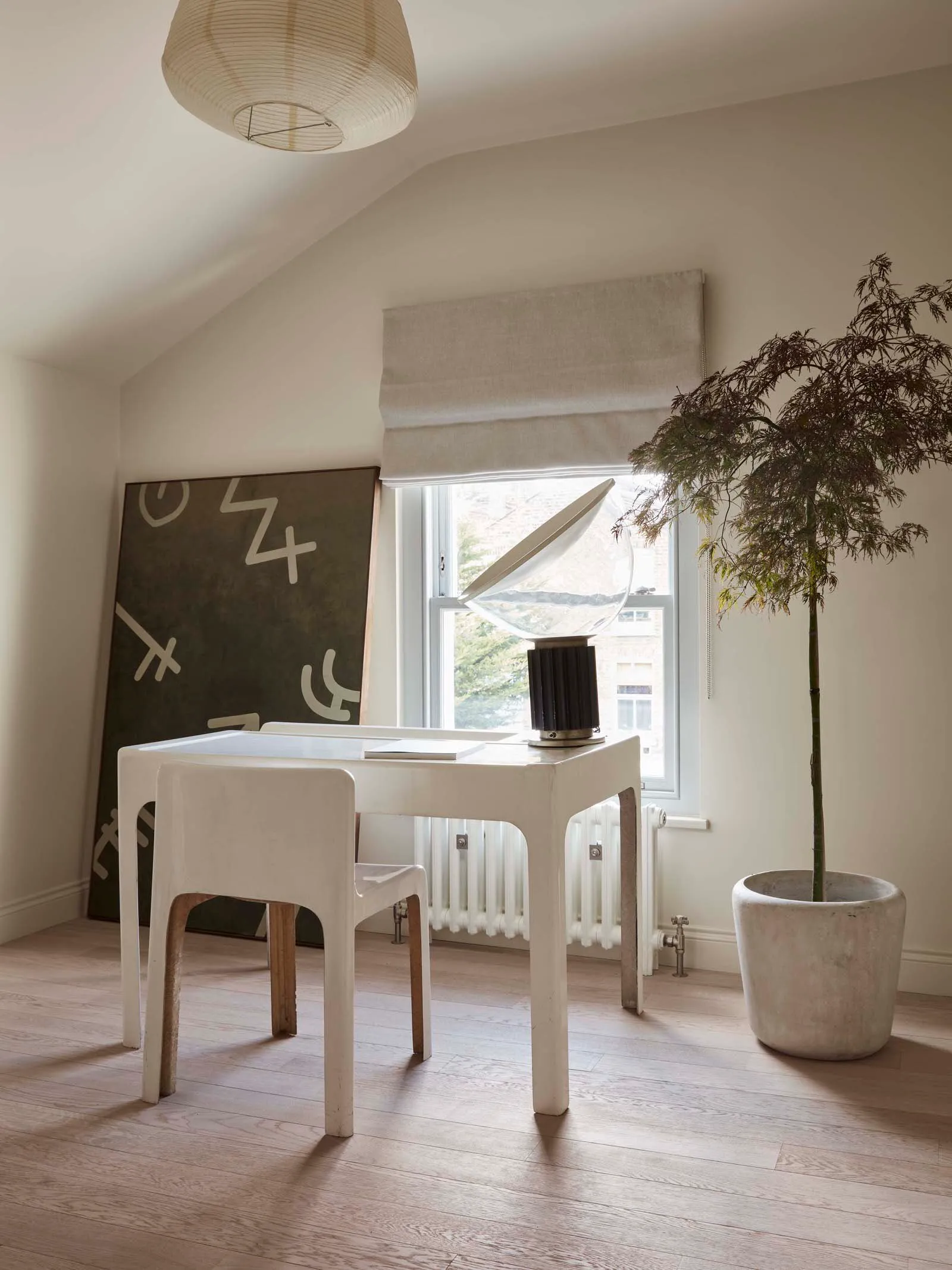 A modern home office with minimalist design, featuring a white desk, chair, and a lamp with a white shade.