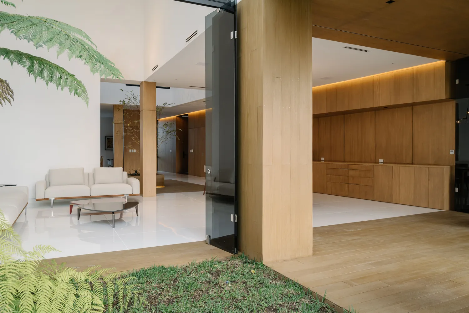 Modern interior design featuring a living room with wooden furniture, white tiles, and plant life.