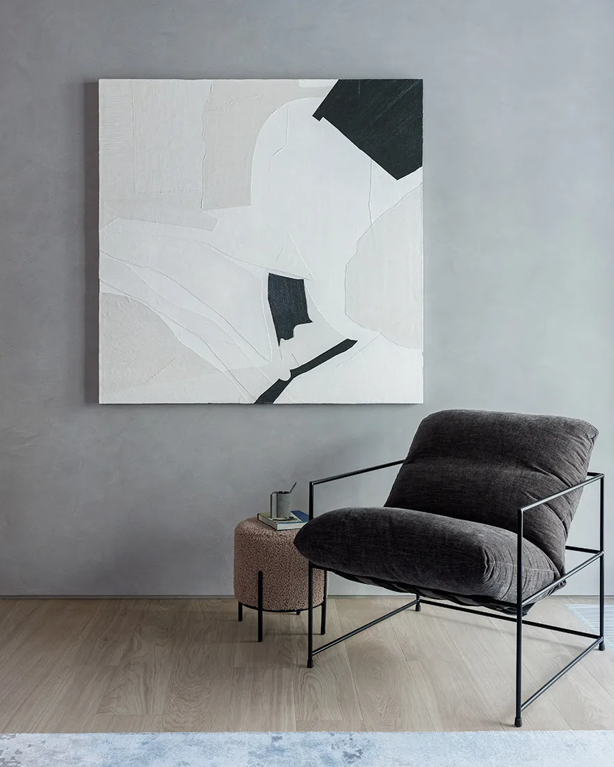 A modern living space featuring a dark upholstered chair with a metal frame, a small side table with a cup and a book, and a 