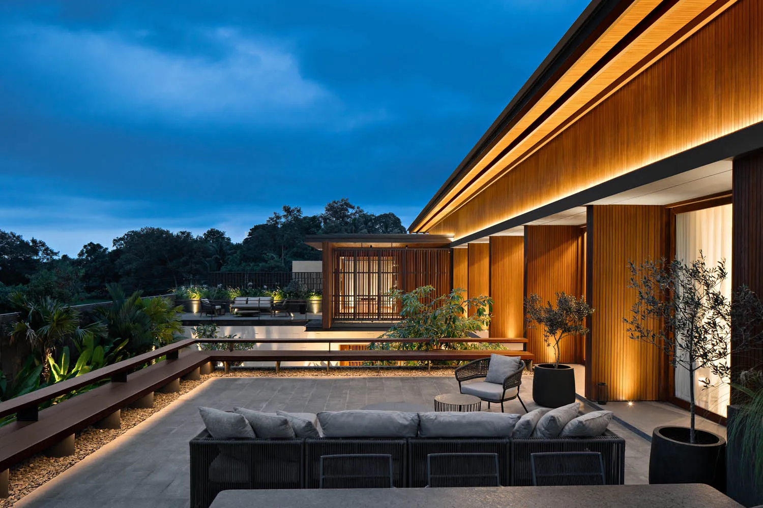 Modern roof deck featuring a cozy seating area with cushioned furniture, illuminated by warm lighting, surrounded by greenery