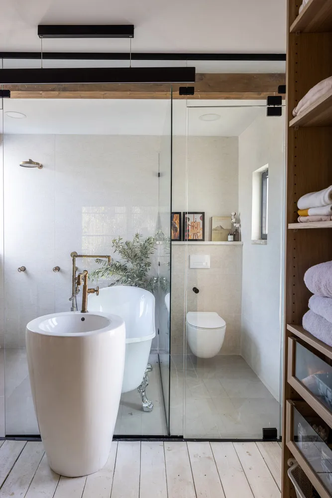 Modern bathroom with a white freestanding tub, glass-enclosed shower, and wooden flooring.
