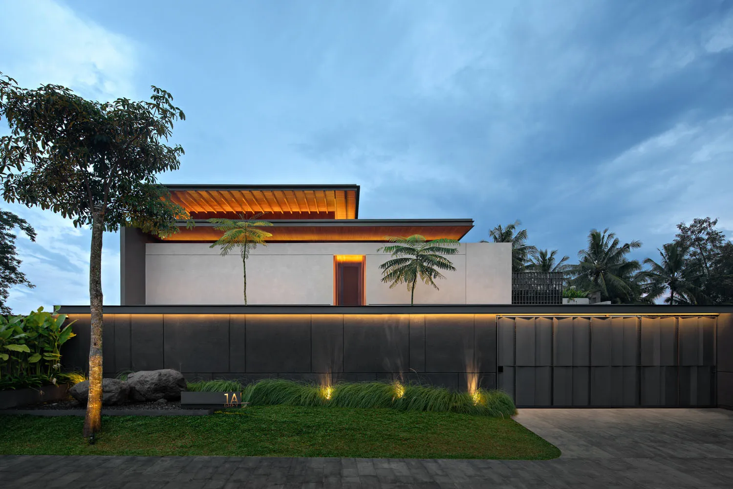 Modern house with concrete exterior at dusk with illuminated pathway and palm trees.