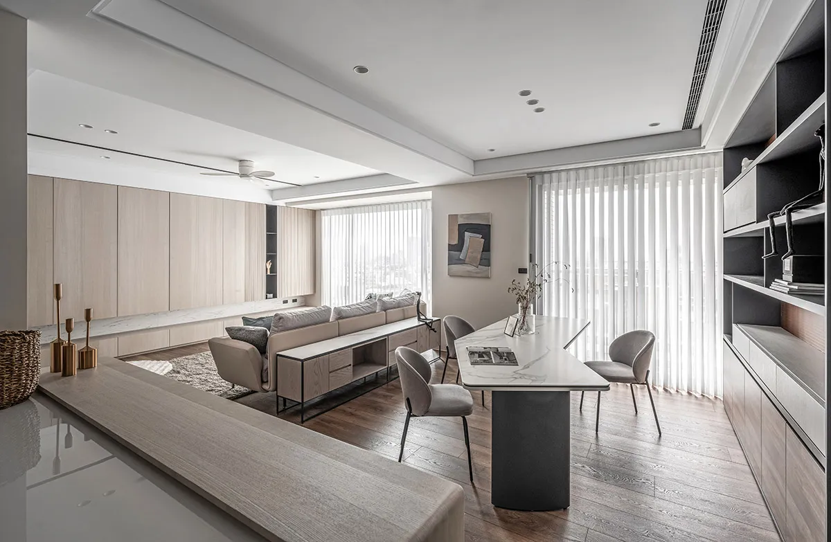 Modern minimalist living room with light wood furniture, gray sofa, and large windows with vertical blinds.