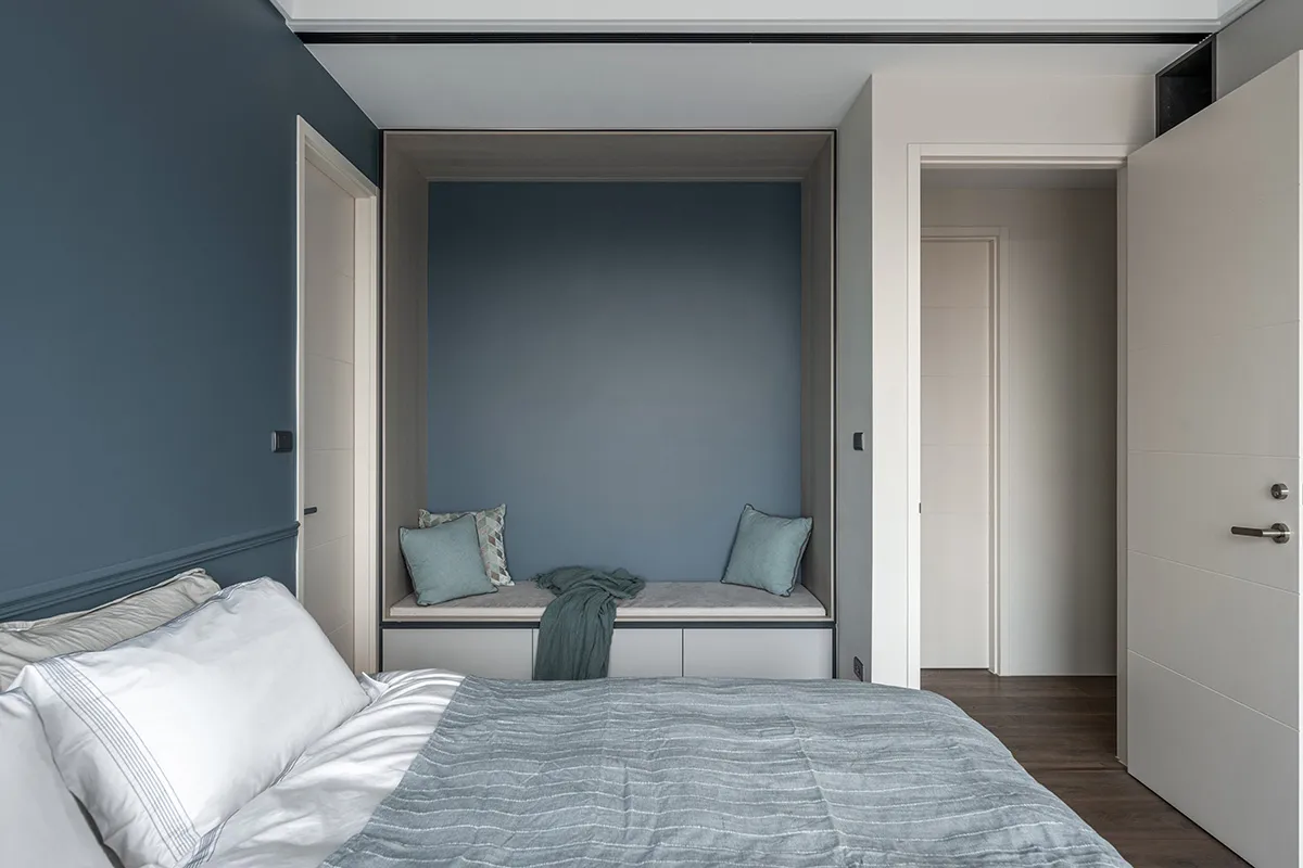 A minimalist bedroom featuring a comfortable seating nook with textured soft furnishings, including a grey bedspread and cush