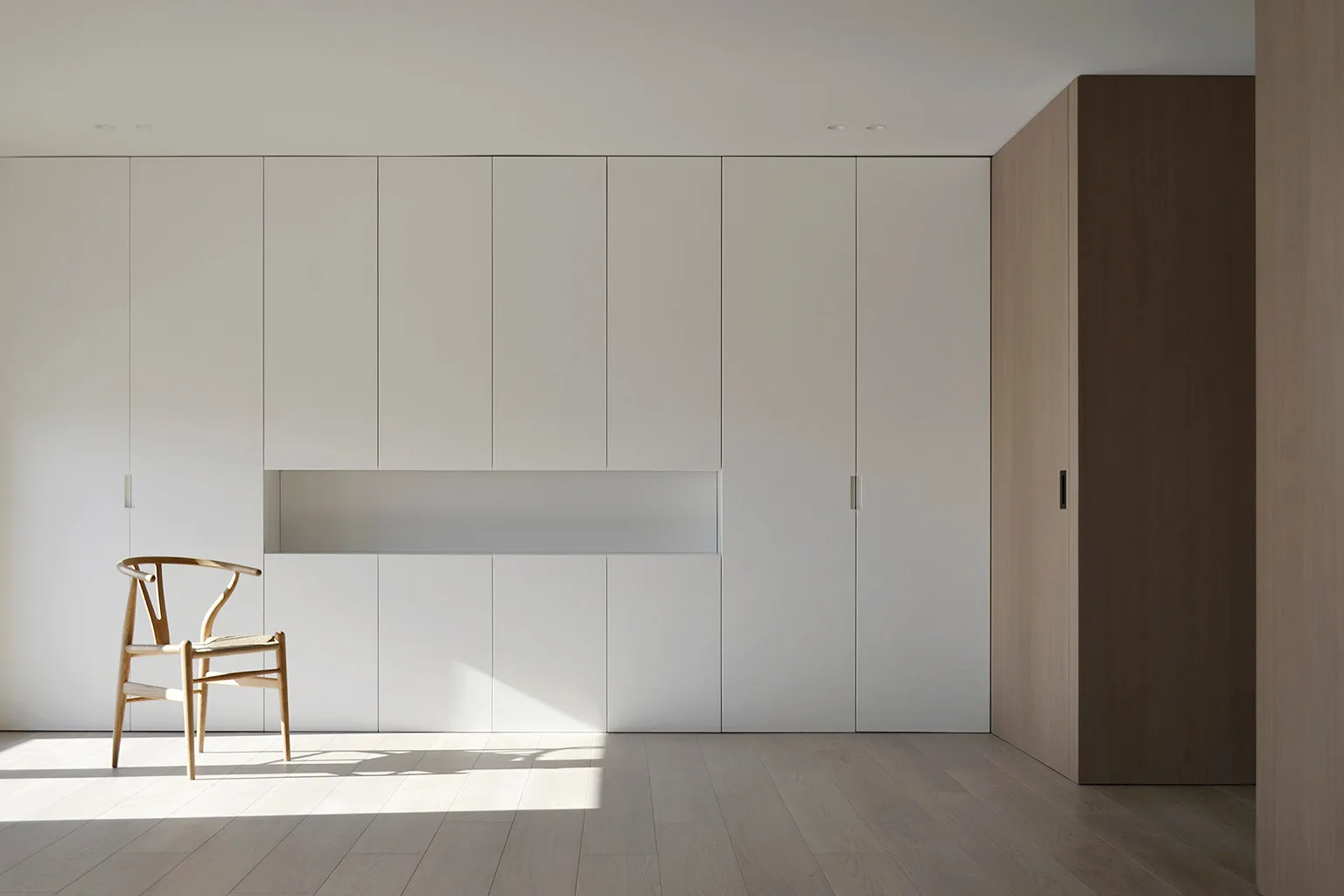 Minimalist-style interior space with wooden cabinets and a Wishbone Chair.