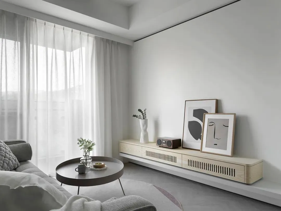 Neutral-toned minimalist living room with white curtains, round coffee table, and abstract artwork on the wall.