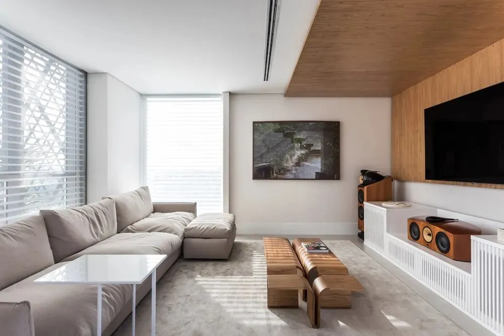 A modern living room with concrete flooring, a beige sectional sofa, and a wooden TV stand with a flat-screen TV.