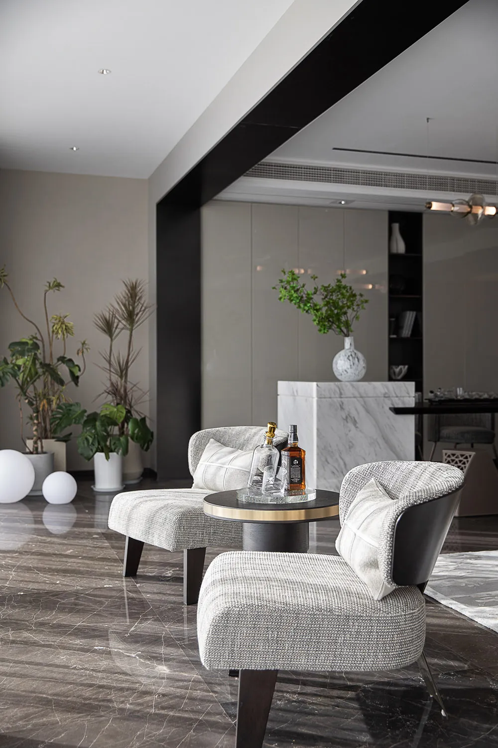 Modern living room with marble floor, grey upholstered chairs, and a round side table with drinks.