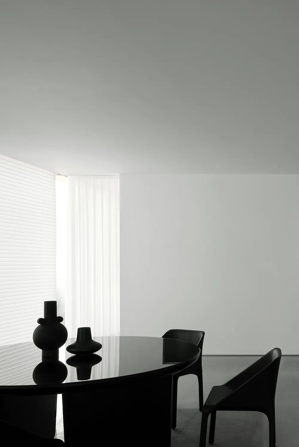 Modern minimalist dining room with glass table and black chairs, featuring a clean, uncluttered aesthetic.