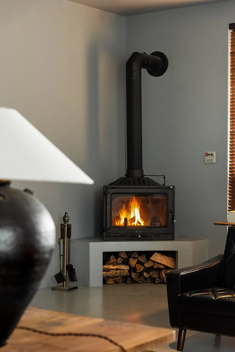 A modern industrial-style living room featuring a freestanding stove with a high chimney and a wood storage area below, surro