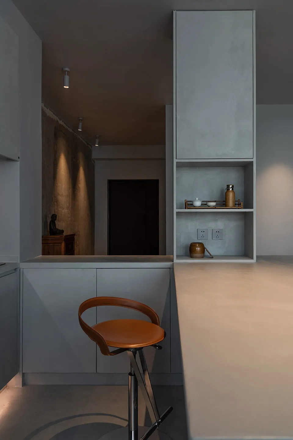 A minimalist residential kitchen featuring concrete countertops and a leather stool.