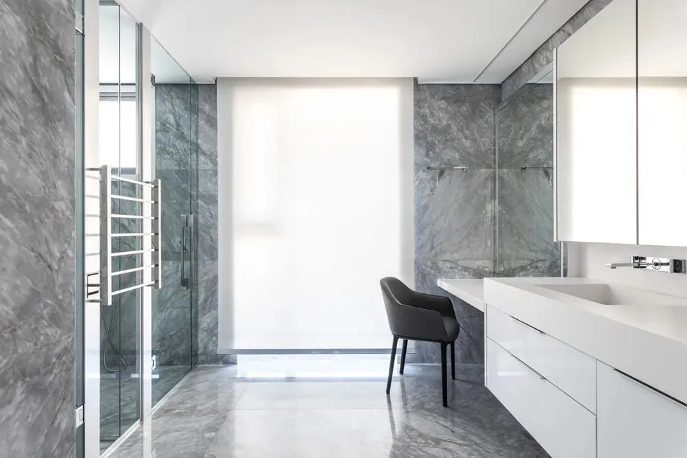 Modern minimalist bathroom with marble walls and floor, glass shower enclosure, and white vanity.
