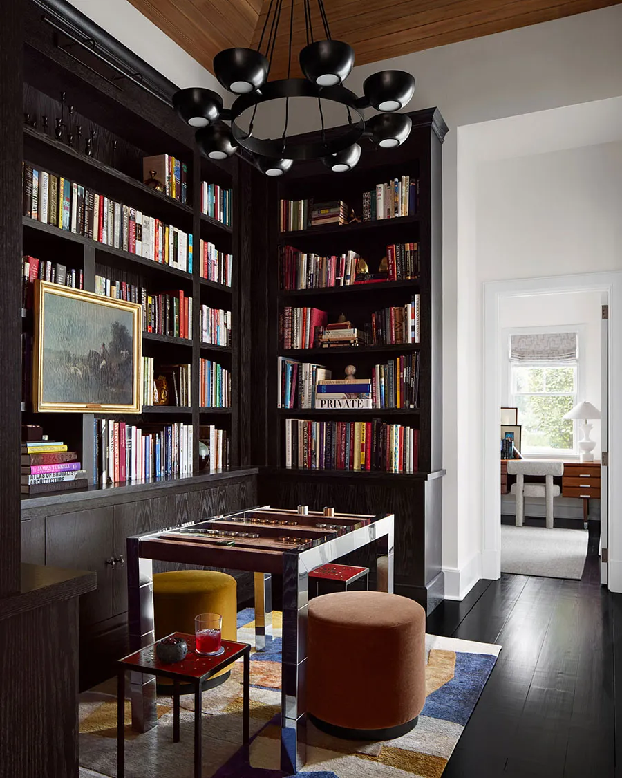 A modern bookshelf library with dark hardwood flooring and a chandelier.