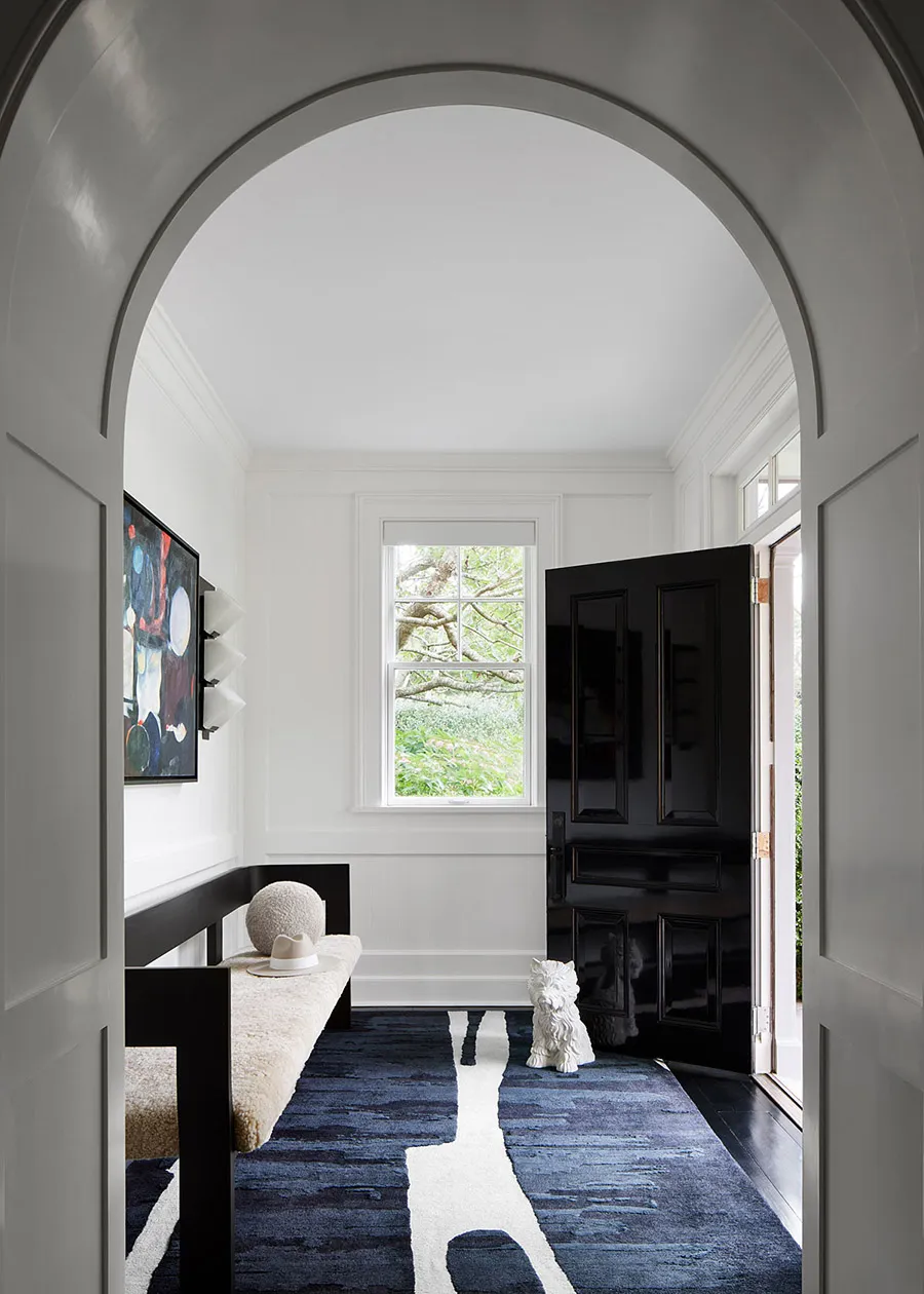 An elegantly designed entrance hall featuring a bold blue rug with white patterns, a wooden bench, and a black front door.