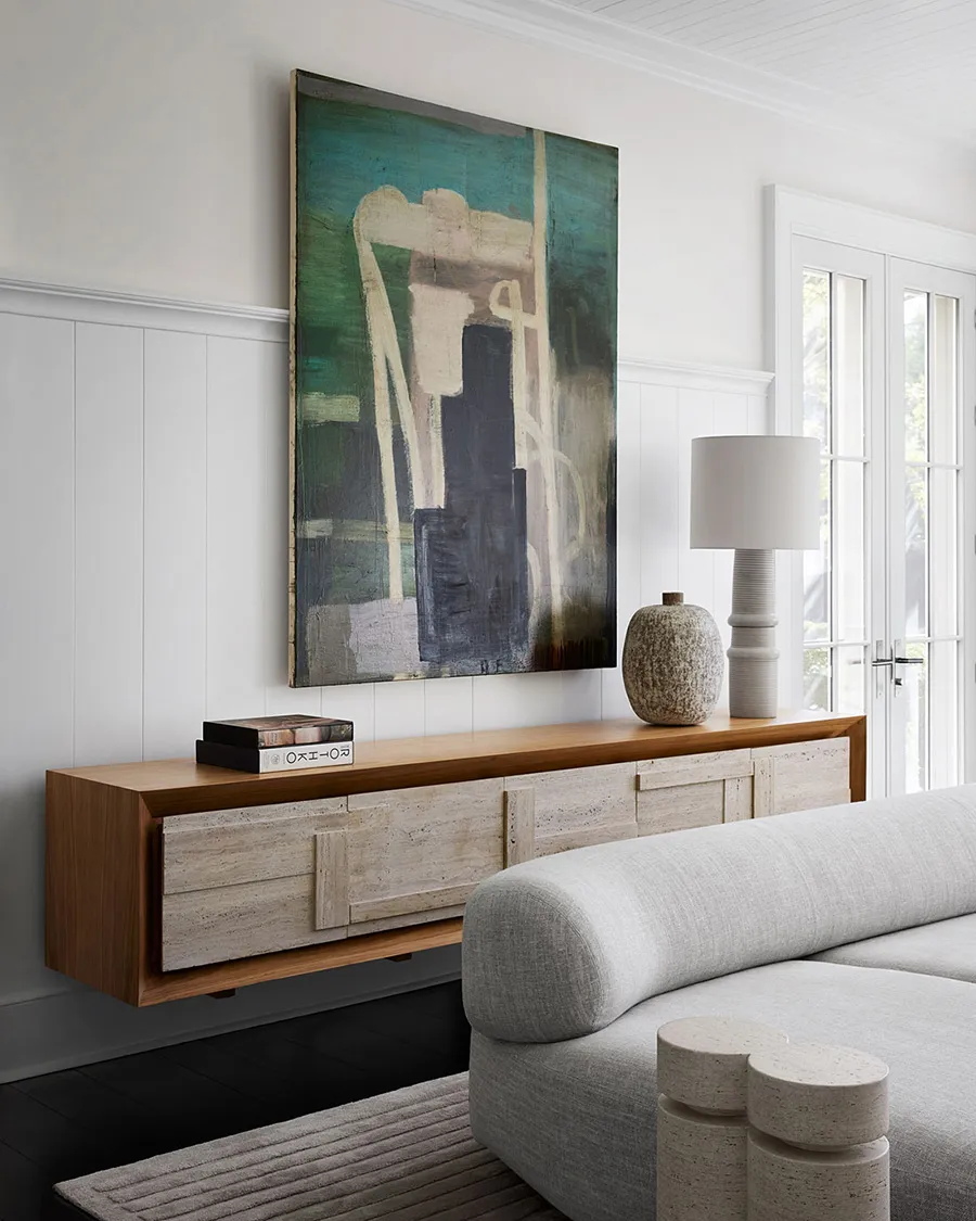 A modern floating console table with a large abstract painting above, minimalistic white sofa, and a lamp.