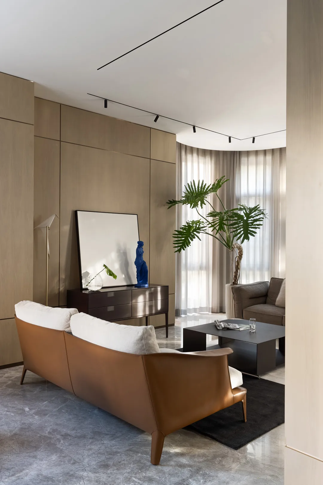 A minimalist living room with a comfortable leather sofa and a sleek coffee table, featuring large windows and modern decor.