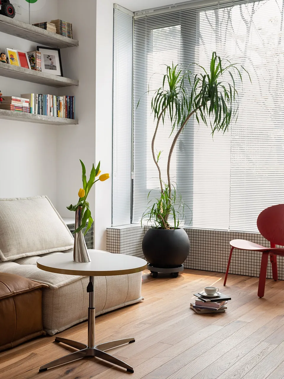 A minimalist living room with a plant, window, and sunlight coming through, featuring tulips in a vase on a table.