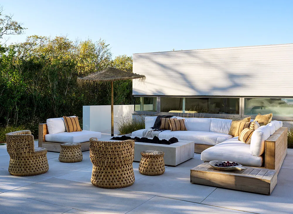 An outdoor residential patio featuring minimalist furniture, including a white sectional sofa, woven rattan chairs, and a woo