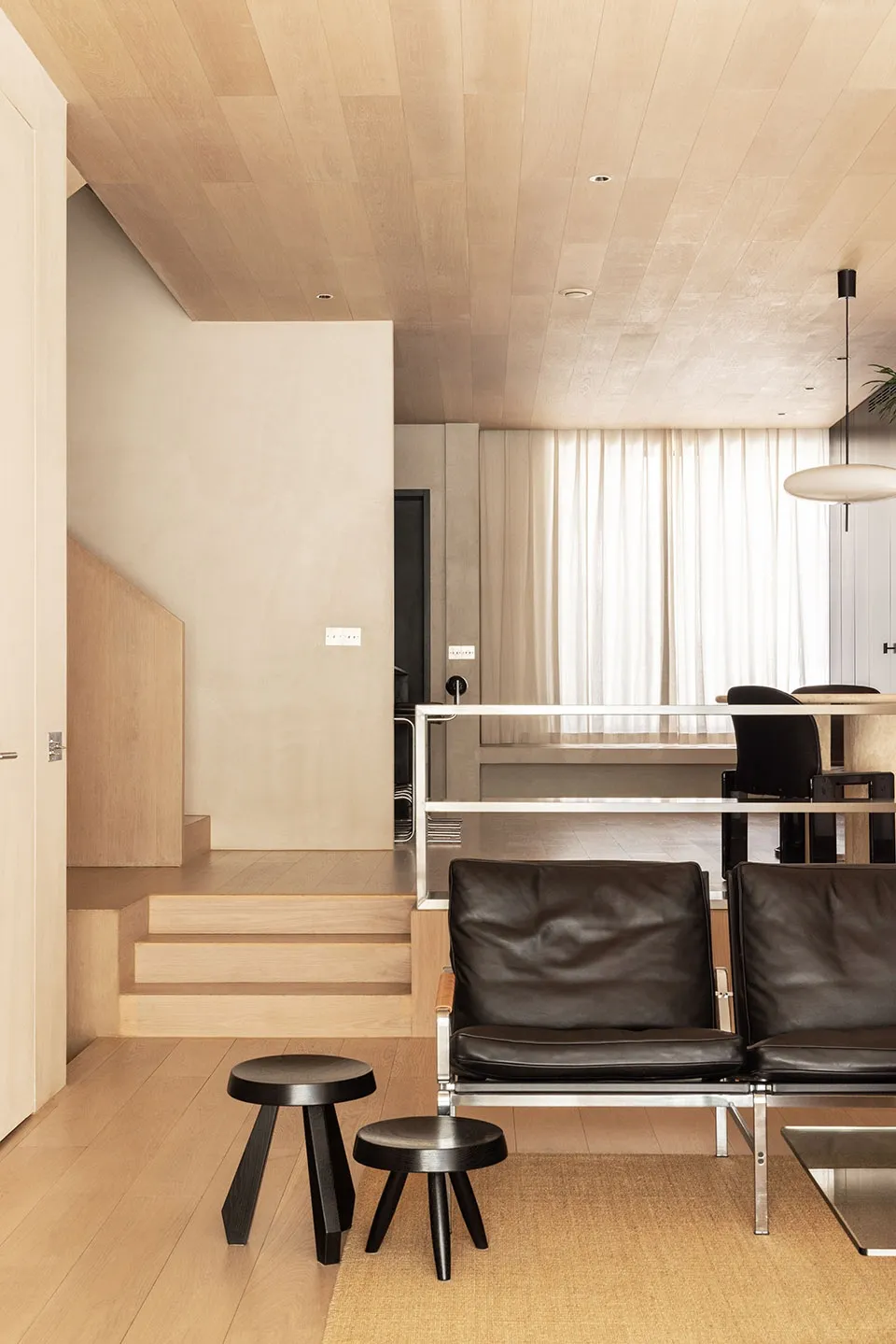 A modern living room with a black leather sofa on a wooden floor, featuring minimalist design elements and neutral colors.