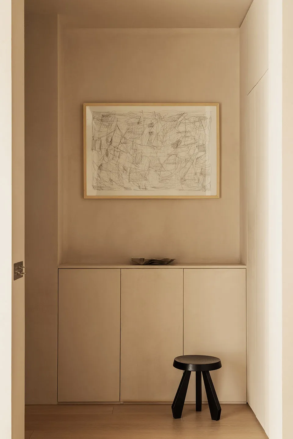 A minimalist entryway featuring neutral-toned cabinets and a black stool.
