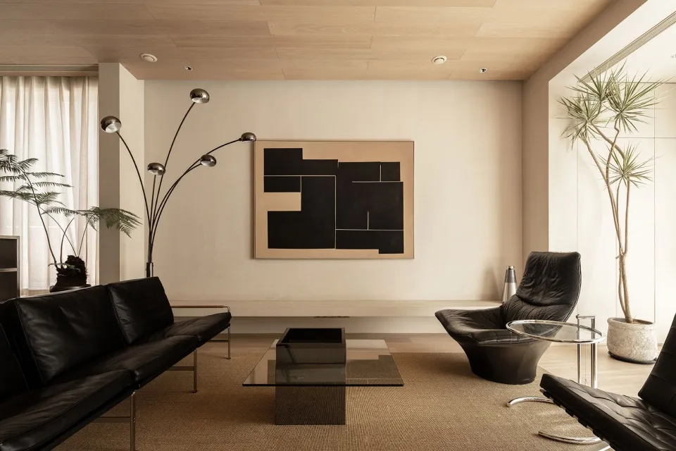 Modern living room featuring a black leather sofa, a glass coffee table, and a wooden coffee table with a geometric black and