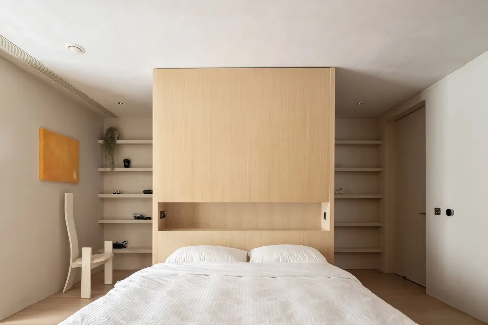 A minimalist bedroom with a wooden wall, white bedding, and floating shelves.