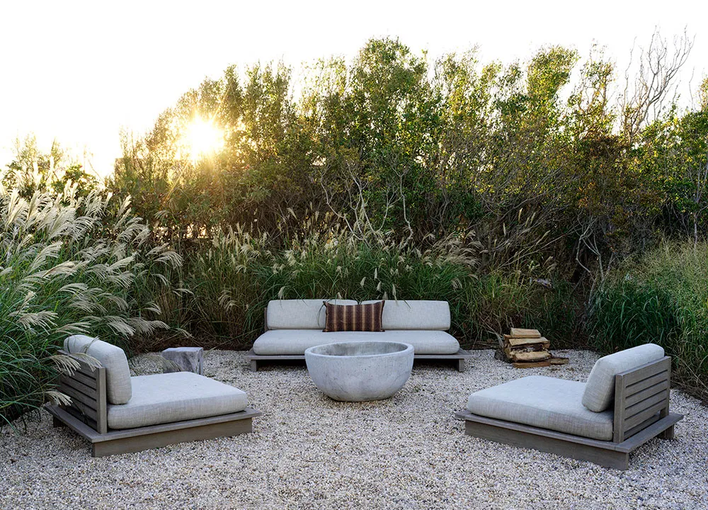 A modern outdoor living space featuring a concrete fire pit surrounded by gravel and pampas grass.