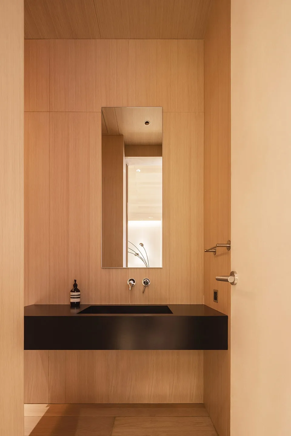 A modern bathroom with a wooden finish, featuring a black countertop and a rectangular mirror above the sink.