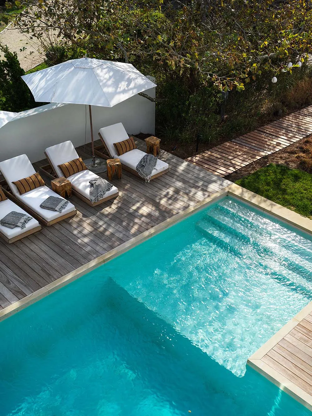 A modern pool deck with wooden deck, glass enclosure, and white lounge chairs.