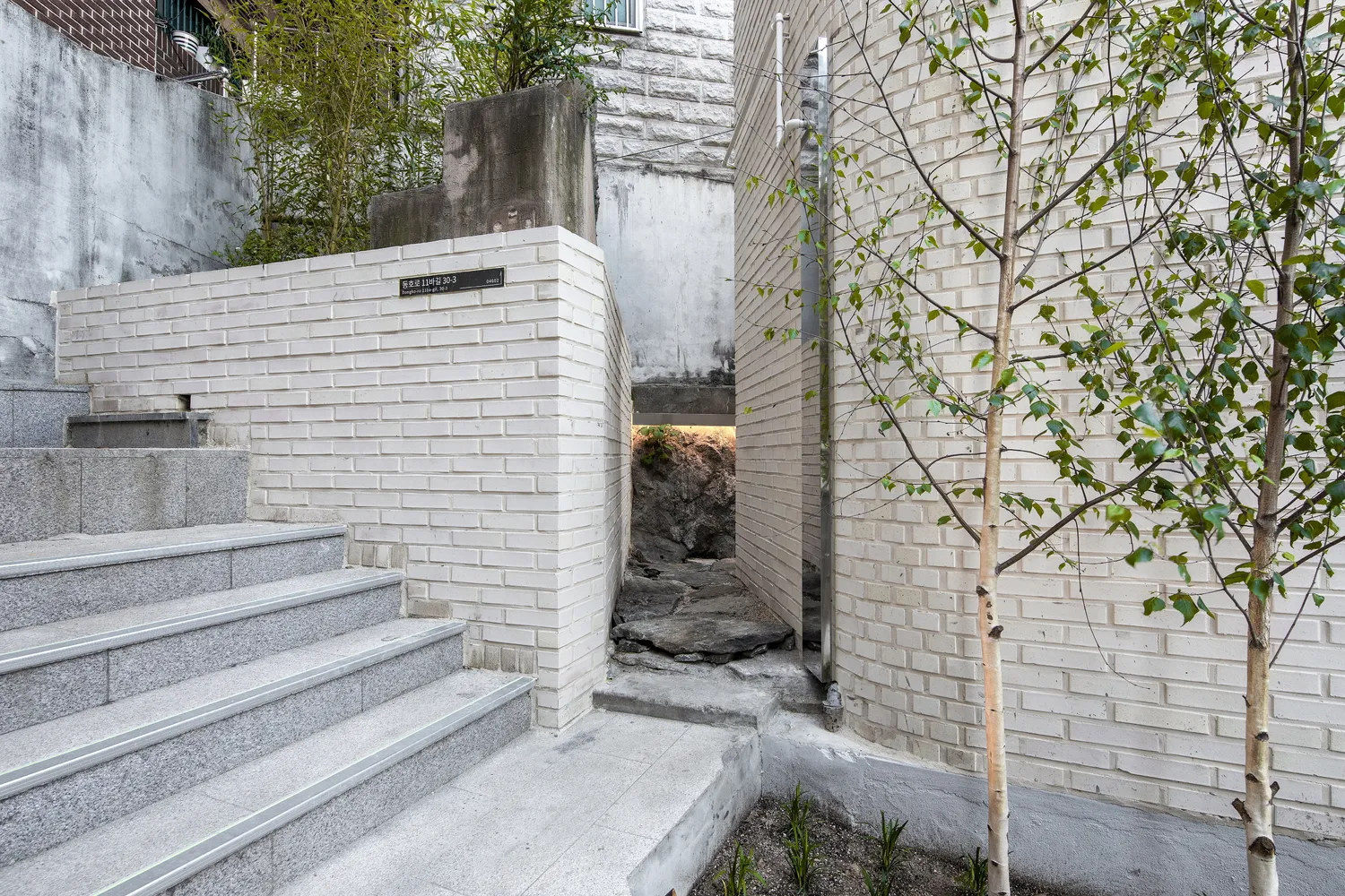 由磚塊與混凝土打造的樓梯，通往住宅建築，兩旁有樹木與植栽。