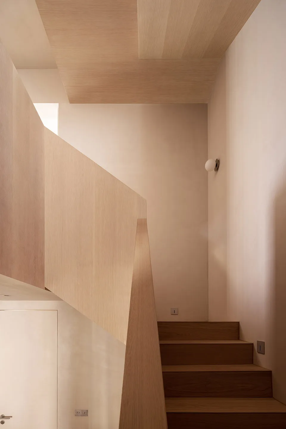 Modern, minimalist interior with wooden staircase and beige walls.