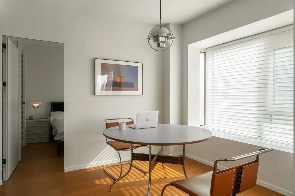 A minimalist home office with a white steel dining table and brown leather chairs.