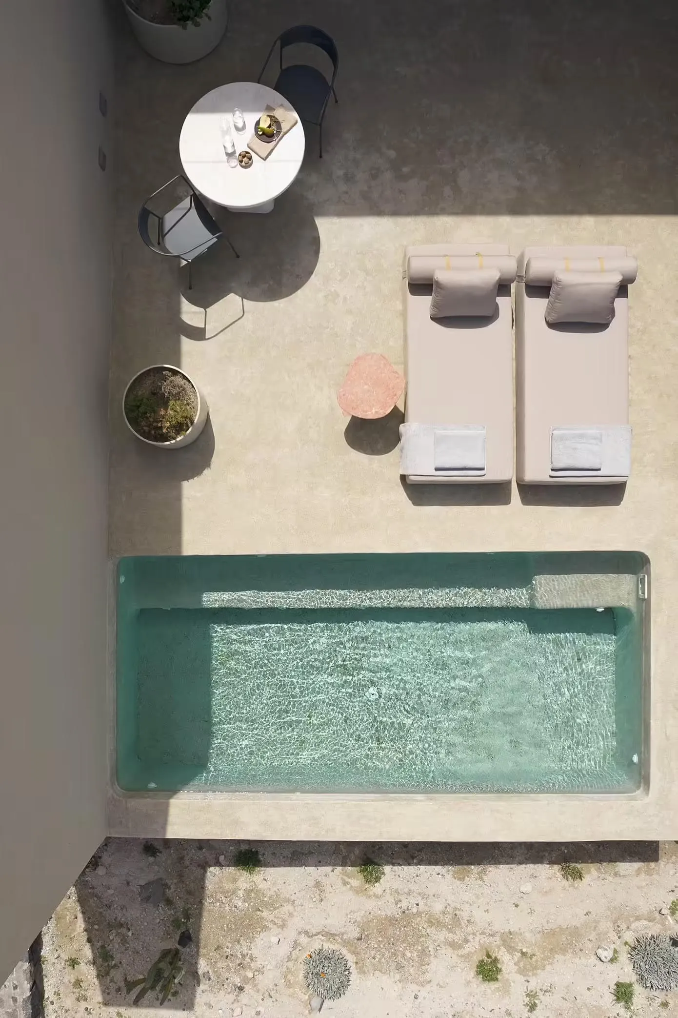 Minimalist outdoor area with a concrete pool, lounge chairs, and dining table.