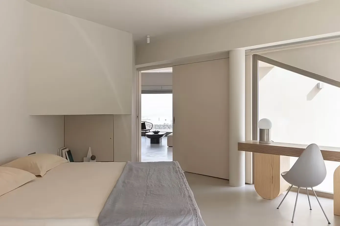 A minimalist bedroom with white furniture and a grey bedspread.